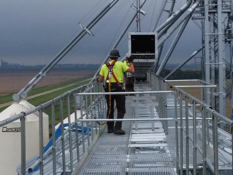Grain systems technician inspecting bin equipment from an elevated catwalk